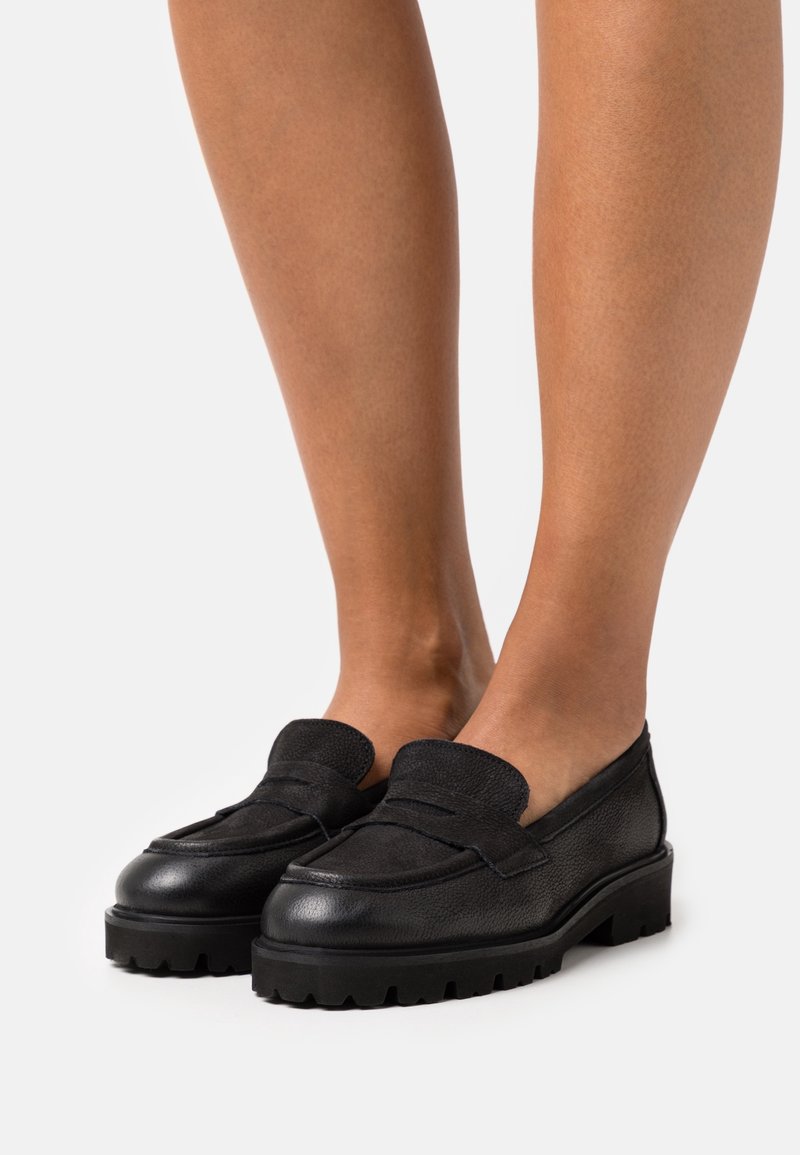 Mocassins en cuir noir avec une finition texturée, dotés d'une bande frontale prononcée et de semelles en caoutchouc épaisses et robustes.
