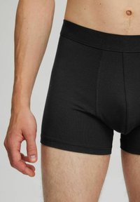 Schwarze Baumwoll-Boxershorts mit flexiblem Bund, taillierter Form und Flachnähten. Der Stoff wirkt glatt mit einem leichten Glanz.