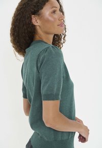 Pulover s kratkimi rokavi temno zelene barve iz pletenine z okroglim izrezom, ki ima diskretno nabrekle rokave in oprijet silhueto v predelu pasu.