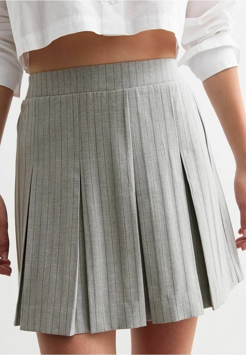 Jupe plissée grise à rayures verticales, dotée d'une taille haute et d'un tissu texturé. Des plis latéraux ajoutent du mouvement et du détail.