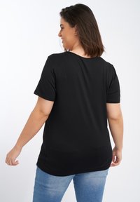 Zwart t-shirt met korte mouwen van een zachte stof, met een ronde halslijn en een iets losse pasvorm, gecombineerd met lichtblauwe jeans.