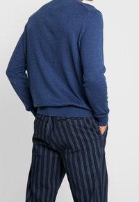 Blå stickad tröja med rund halsringning, kombinerad med mörkblå kostymbyxor med ränder. Mjuk textur, avslappnad passform, synliga sidofickor.