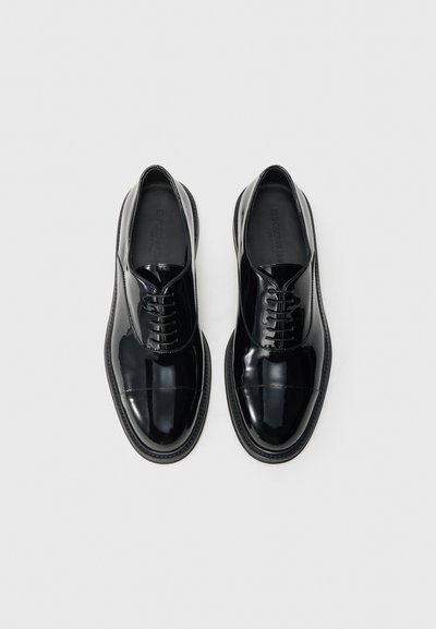 Fekete, fényes bőr fűzős cipők sima felülettel, lekerekített orral és kontrasztos talppal. Finom varrásokkal és struktúrált fűzőkkel rendelkeznek.