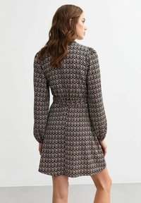 Robe à motifs noir et blanc avec des manches longues, une taille cintrée et un design à lignes ondulées, présentant une taille cintrée et une jupe évasée.