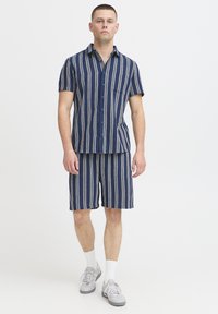 Košeľa s krátkym rukávom na gombíky a zodpovedajúce šortky v námorníckej modrej farbe s viacfarebnými vertikálnymi pruhmi; vyrobené z textúrovaného materiálu; ležérny strih.