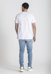 Bílý bavlněný tričko s krátkými rukávy, spárované s světle modrými džíny. Džíny mají slim fit a mírné oděrkání na kolenou.