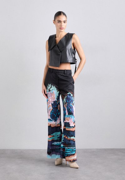 Svart lærcrop vest med en omslagsdesign, kombinert med vide bukser med et fargerikt abstrakt mønster i blått, rosa og brunt.