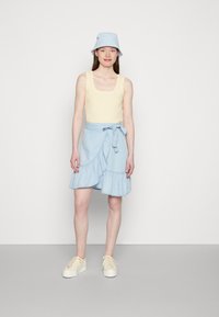 Top de malha amarelo claro com bordas em forma de onda, combinado com uma saia envolvente azul claro com bainha em babados e cintura amarrada. Ténis brancos.