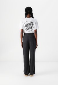 Un t-shirt blanc à manches courtes avec un graphique noir "Santa Cruz", associé à un pantalon noir ample et des chaussures claires.