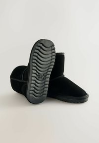 Schwarze Wildleder-Ankle Boots mit einer flachen Gummisohle mit geriffeltem Muster. Abgerunde Zehenpartie und einfache Stichdetails an den Seiten.