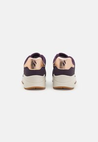 Chaussures violettes avec un col rembourré, accents métalliques en or rose sur le talon, semelle blanche et semelle extérieure en caoutchouc texturé pour une meilleure adhérence.