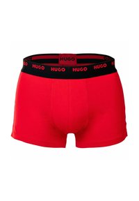 Red boxer shorts made of cotton with a black elastic waistband, featuring repeating "HUGO" logo text in red.