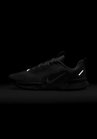 Black Nike running shoe featuring a textured upper, reflective accents, curved shape, and a treaded sole designed for traction.