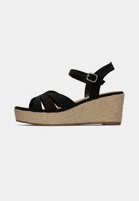 Les sandales compensées noires présentent des brides croisées en tissu, une bride de cheville réglable, et une plateforme en jute tissé texturé pour une hauteur supplémentaire.