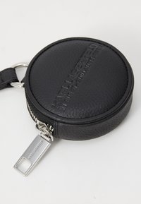 Rundes, schwarzes Leder-Münzfach mit strukturierten Oberflächen, geprägtem Logo, silbernem Reißverschluss und metallener Schlüsselring-Befestigung.