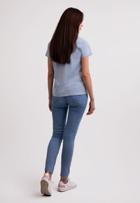 Svetle modré tričko s krátkým rukávem v kombinaci se svetle modrými slim džínami a bílými teniskami, s jednoduchou, hladkou texturou a ležérním designem.