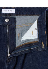 Jeans in denim scuro con un interno in tessuto blu. Presentano una zip metallica, cuciture a contrasto e un'etichetta con testo giapponese nella cintura.