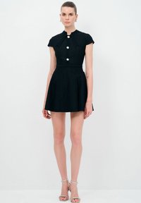 Schwarzes Kleid mit hohem Kragen, kurzen Ärmeln und tailliertem Oberteil. Verfügt über drei große Knöpfe und einen schwingenden Rock. Glatte Textur.