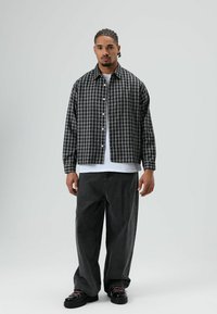 Zwart-grijs geruit overhemd met knopen, losse donkergrijze spijkerbroek, zwarte veterschoenen, gedragen over een wit T-shirt.