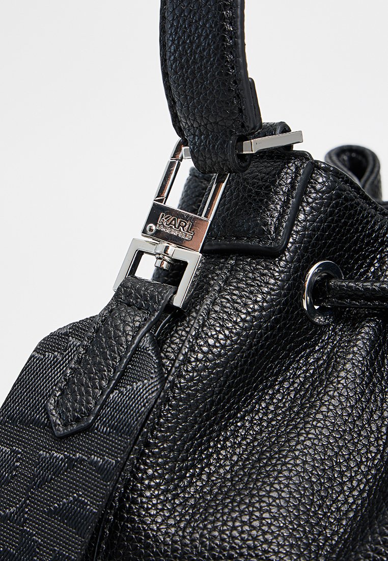 Schwarze Lederhandtasche mit strukturiertem Finish, silbernem Beschlag und Logo-Verschluss. Enthält einen abnehmbaren Schulterriemen und einen Kordelzugverschluss.