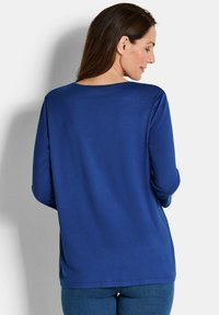 Langärmliges Hemd aus tiefblauem Stoff, mit einem schlichten Rundhalsausschnitt und lockerer Passform sowie einer glatten Textur.