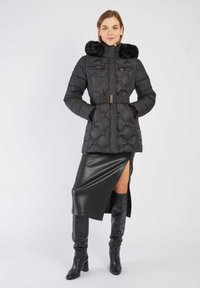Czarna pikowana kurtka puchowa z kapturem z sztucznego futra, z paskiem w talii i zamykanymi kieszeniami. Noszona na czarnej skórzanej spódnicy midi z bocznym rozcięciem.