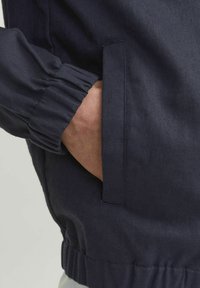 Tume sinine jakkk, millel on elastsed mansetid ja küljetasku. Materjal näeb välja tekstuurne, esitledes iga päevast disaini.