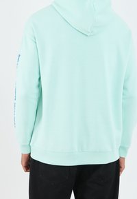 Mintgrön hoodie med dragsko i huvan, ribbade ärmar och fåll. Har en djärv blå grafisk tryck längs vänster ärm. Tillverkad av bomullsmaterial i blandning.
