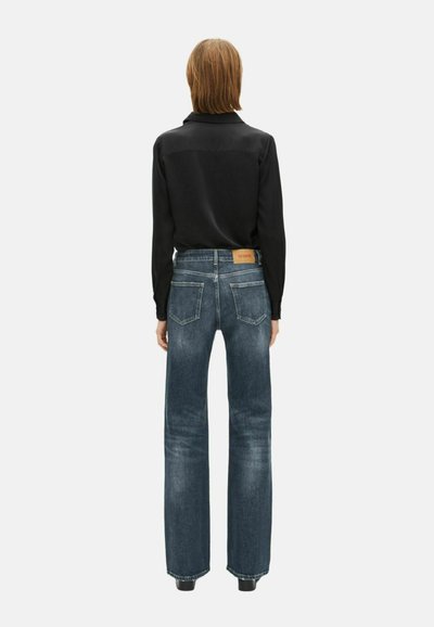 Camisa negra de manga larga combinada con jeans azul de tiro alto y pierna ancha, que cuentan con un parche de cuero marrón en la parte trasera.