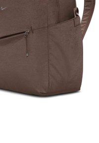 Bolsa de tela marrón con un diseño elegante, bolsillo con cremallera y un logo sutil. La textura parece suave con una forma estructurada.
