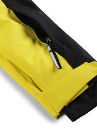 Giacca in tessuto nera e gialla con tasca con zip, caratterizzata da una superficie liscia e sezioni di colore contrastante. Sono visibili i polsini rinforzati.