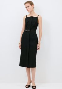 Schwarzes tailliertes Kleid mit Spaghettiträgern, einem quadratischen Ausschnitt, einem Gürtel in der Taille und seitlichen Taschen. Glattes Gewebe in Midilänge.