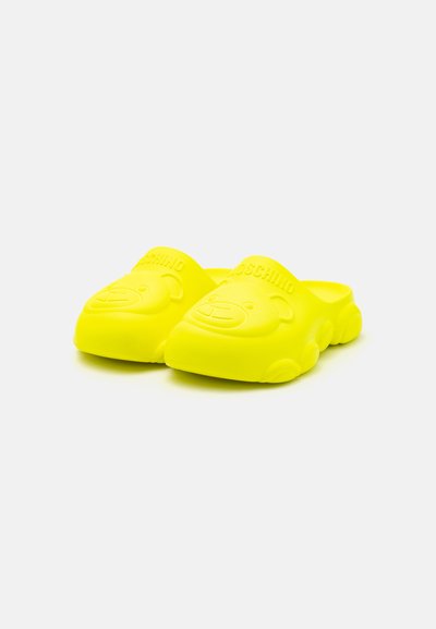 Zuecos de goma amarillos brillantes con una cara de osito moldeada en el frente y acentos texturizados, con un diseño sin cordones.