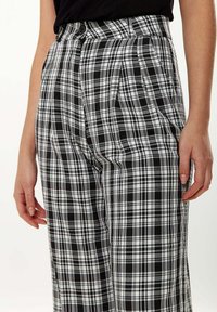 Black and white plaid trousers with a loose fit, featuring a pleated front and two side pockets. Fabric has a smooth texture.