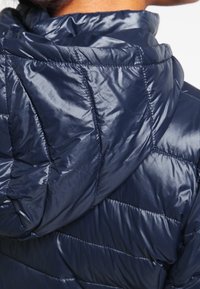 Náměťná modrá péřová bunda s lesklou prošívanou texturou a kapucí. Obsahuje horizontální švy a hladký povrch.