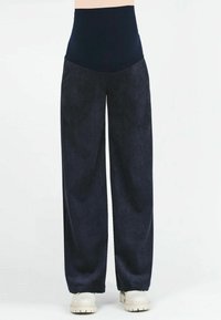 Pantaloni a gamba larga in corduroy blu marina con una vita alta. Texture morbida e motivo a coste. Abbinati a sneakers di colore chiaro.