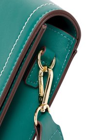 Taschen-Ecke aus tealfarbenem Leder, mit weißem Nähen, goldenen Beschlägen und einem abnehmbaren Gurt mit Lederakzenten.