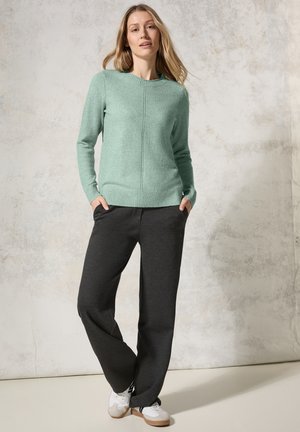 Suéter de punto verde menta con un cuello acanalado, combinado con pantalones de chándal holgados de color gris oscuro y zapatillas blancas sobre un fondo claro.