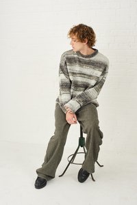 Raštuotas, įvairių spalvų megztinis su pilkais ir grietinėlės atspalviais, derinamas su žaliais platėjančiais trikotažo kelnių ir juodais batais.