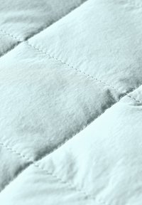 Jasnoniebieska tkanina pikowana o miękkiej teksturze, z widocznymi wzorami w formie pudełek i widocznym ściegem, podkreślająca jej izolowaną konstrukcję.