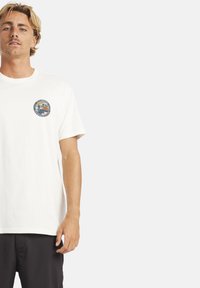 Weißes Baumwoll-T-Shirt mit einem runden Grafiklogo auf der linken Brust. Kurze Ärmel und lockere Passform. Leichter Stoff mit glatter Textur.
