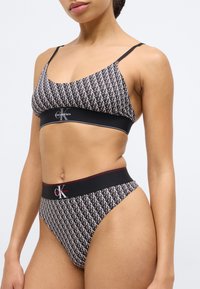 Σετ σουτιέν bralette και σλιπ με ψηλή μέση Calvin Klein σε ασπρόμαυρο με επαναλαμβανόμενο μοτίβο λογότυπου, με ρυθμιζόμενους ιμάντες και ελαστικές ζώνες στη μέση.