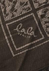 Mørkebrunt tekstil med et vevet design i beige aksenter. Stoffet er mykt med en teksturert overflate og har broderte detaljer.