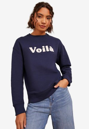 Námornícky modrý sveter vyrobený z bavlnenej látky s okrúhlym výstrihom a rebrovanými manžetami, na prednej strane s vyšitou slovom "Voilà" v svetlej farbe.