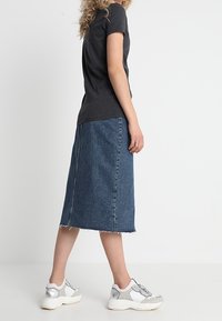 Šedé tričko s krátkým rukávem, modrá džínová midi sukně s třepeným lemem a stříbrné sportovní tenisky s bílými akcenty a texturovanou podrážkou.