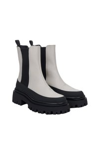 Masivní kotníkové boty s krémovým koženým svrškem, černými elastickými panely a silnou černou gumovou podrážkou s hlubokými drážkami pro trakci.