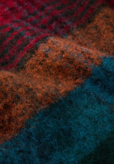 Textured fabric with horizontal sections in red, brown, and teal, featuring a soft and fuzzy appearance, with varying color intensities.