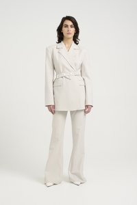 Lys beige skreddersydd blazer med belte i midjen, kombinert med flagrende bukser. Glatt stoff, dobbeltradsfront og minimalistisk design.