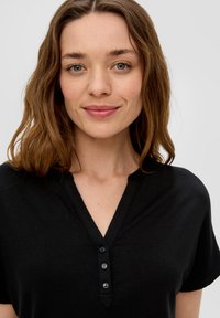 Zwart shirt met korte mouwen, een v-hals en een drieknoopsluiting. Soepele textuur, casual pasvorm en minimalistisch ontwerp.