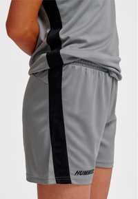 Gråa sportshorts med svart sidostripes, gjorda av lättviktigt material. Har en elastisk midjeresår och "HUMMEL"-logotyp på fållen.